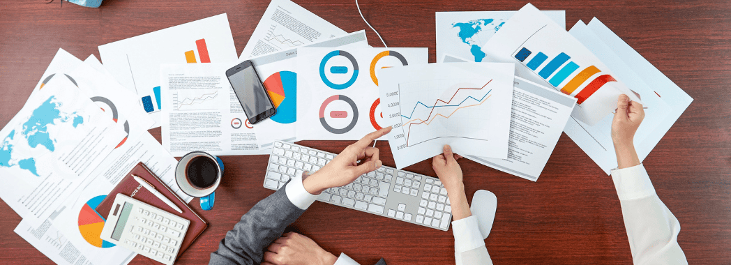 Imprenditori visti dall'alto analizzano grafici di performance per valutare il budget investito in marketing btob